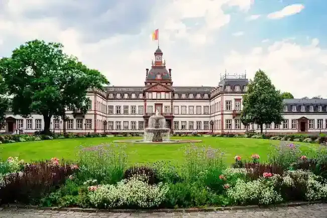 Hanau Schloss Philippsruhe in Hanau mit einem Brunnen und Blumenbeeten vor einer grünen Wiese.