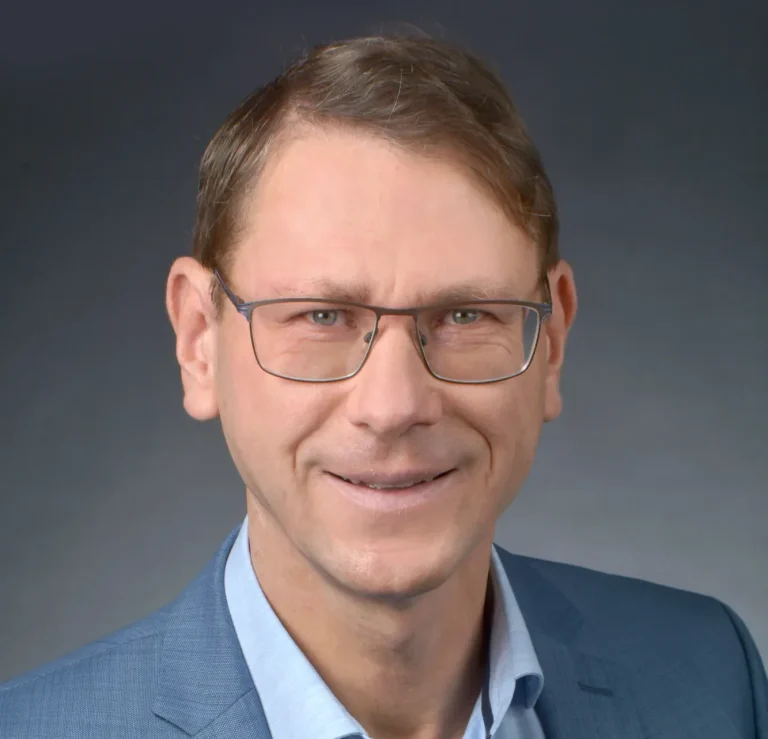 Rechtsanwalt für Insolvenzrecht Karsten Kruschel: mit Brille und Anzug und Hemd, lächelt freundlich vor grauem Hintergrund.