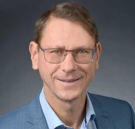 Rechtsanwalt für Insolvenzrecht Karsten Kruschel: mit Brille und Anzug und Hemd, lächelt freundlich vor grauem Hintergrund.